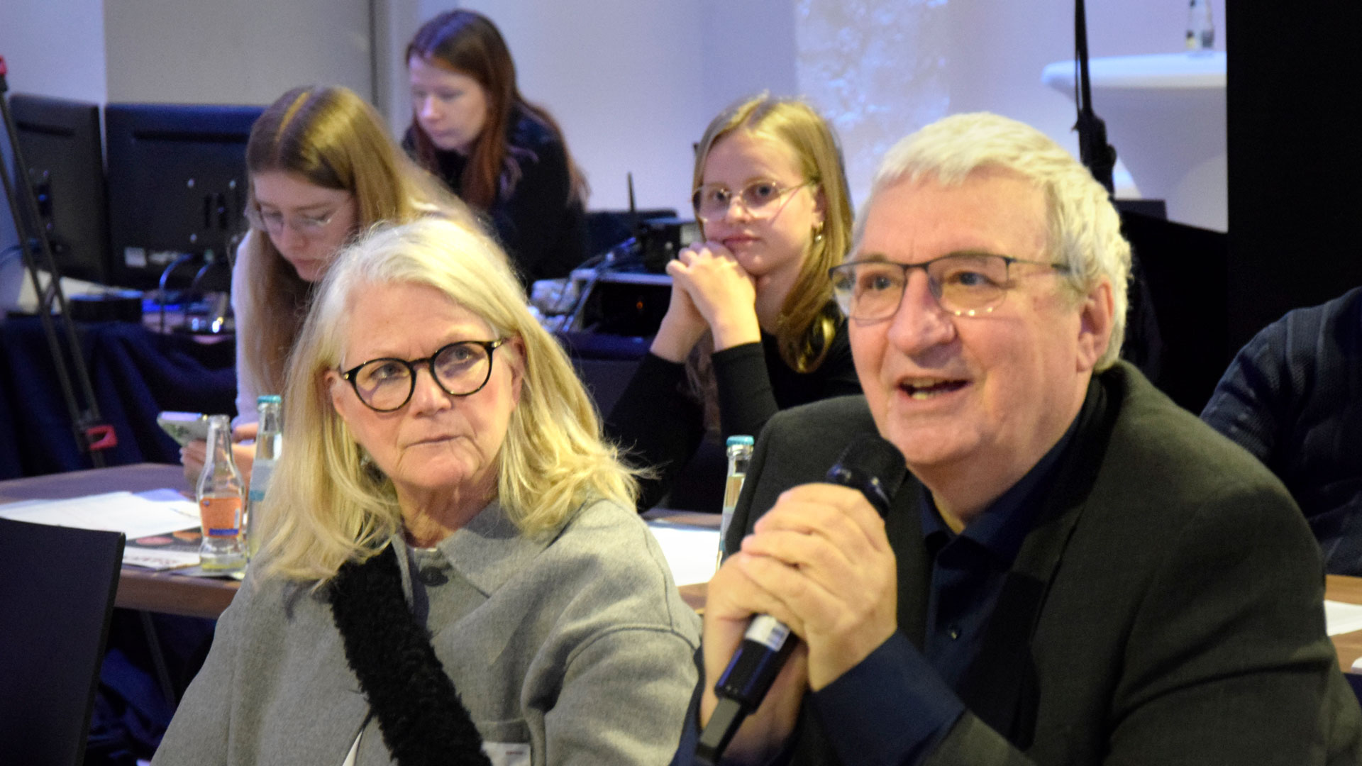 Frage aus dem Publikum - Mann mit Mikrofon sitzend im Plenum