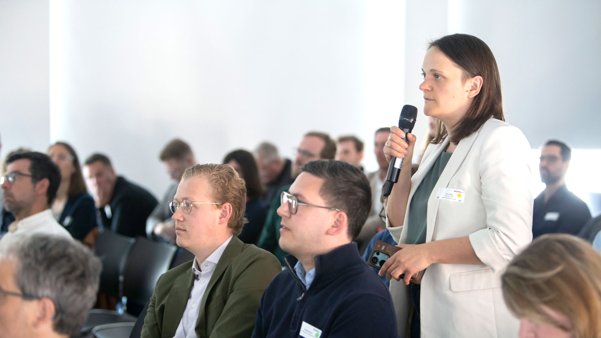 Frage aus dem Publikum: Dame stehend mit Mikrofon, umrandet von Plenum. 